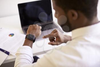 Businessman Working On Laptop At Desk In Modern Office Checking Data On Smart Watch