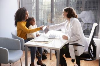 Female Pediatrician Shaking Hands With Mother And Daughter Meeting In Hospital Office