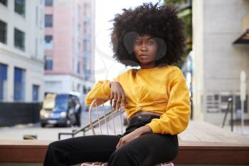 Young black woman with afro hair and yellow top sitting on a chair in the street looking to camera