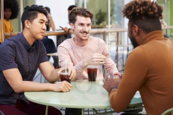 Three millennial male friends talking over cold brews outside a cafe in a city street, close up