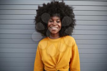 Young black woman with afro standing against grey security shutters, smiling to camera, close up