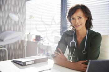Portrait Of Smiling Female Doctor With Stethoscope Sitting Behind Desk In Office
