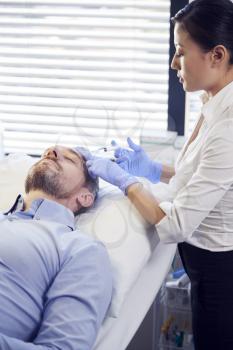 Female Beautician Giving Mature Male Patient Botox Injection In Forehead