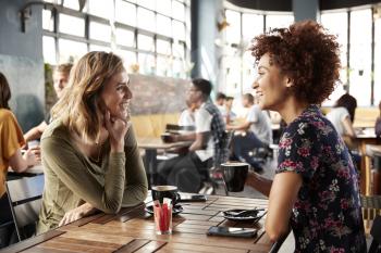 Two Female Friends Meeting Sit At Table In Coffee Shop And Talk