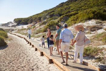 Three generation white family walking together along a wooden promenade on a beach, full length
