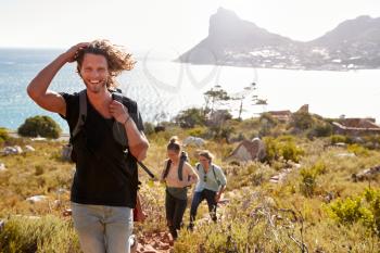 Young adult white man hiking with friends in countryside by the coast smiling to camera
