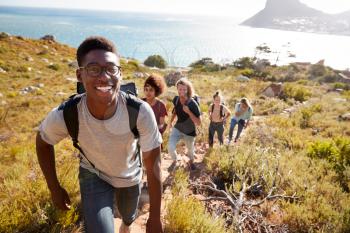 Millennial African American man leading friends hiking single file uphill on a path by the coast