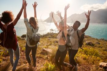 Millennial friends on a hiking trip celebrate reaching the summit, cheering with arms in the air