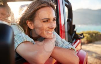 Millennial white woman on a road trip with friends leaning on car door enjoying view, close up