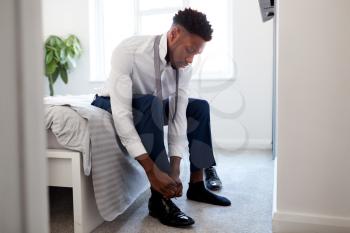 Businessman At Home Sitting On Bed Putting On Shoes Before Leaving For Work