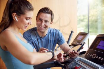 Woman In Gym With Personal Trainer Analysing Performance Using Smart Watch And Digital Tablet