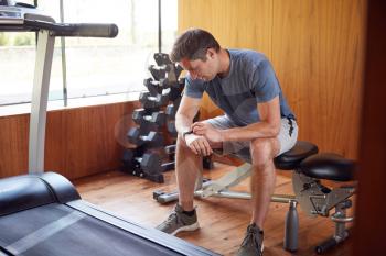 Man Exercising Sitting On Weight Bench In Home Gym Checking Smart Watch