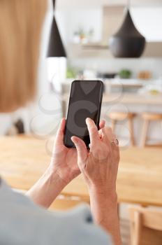 Mature Woman Using App On Mobile Phone To Control Central Heating Temperature In House