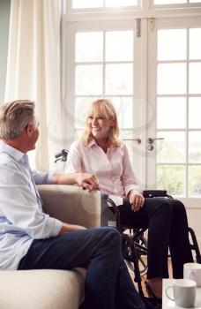 Mature Couple With Woman In Wheelchair Sitting In Lounge At Home Holding Hands Together