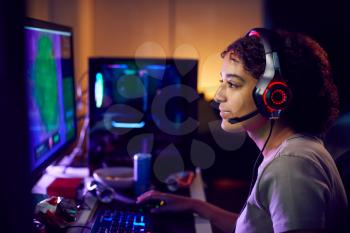 Teenage Girl Wearing Headset Gaming At Home Using Dual Computer Screens