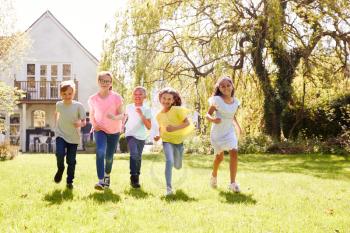 Group Of Children Running Across Garden Lawn At Home Looking Into Camera