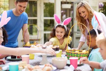 Parents With Children Wearing Bunny Ears Enjoying Outdoor Easter Party In Garden At Home
