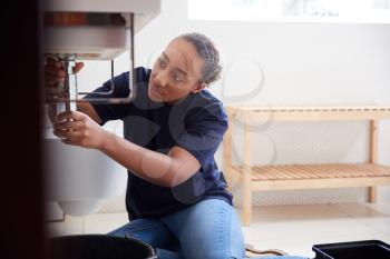 Female Plumber Working To Fix Leaking Sink In Home Bathroom