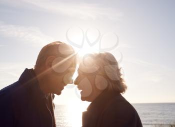 Loving Active Senior Couple Holding Hands As They Walk Through Sand Dunes Against Flaring Sun