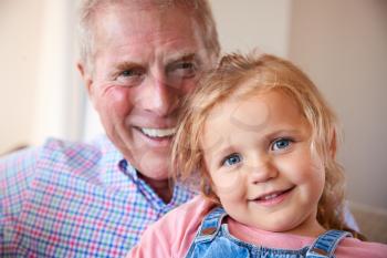 Portrait Of Loving Grandfather Cuddling Granddaughter On Sofa At Home