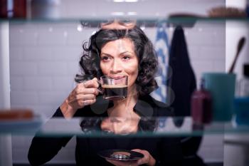 View Through Bathroom Cabinet Of Mature Businesswoman Drinking Coffee