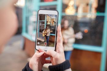 Person Filming Female Musician Busking Playing Acoustic Guitar And Singing To Crowd On Mobile Phone