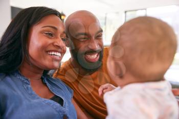 Smiling African American Parents Cuddling And Playing With Baby Daughter Indoors On Sofa At Home