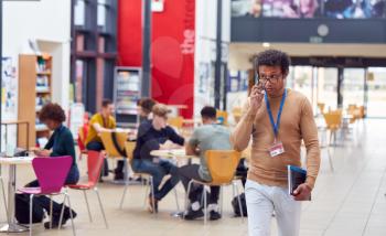 Communal Area Of Busy College Campus With Students Working At Tables And Tutor On Phone