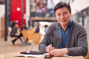 Portrait Of Mature Male Teacher Or Student With Digital Tablet Working At Table In College Hall