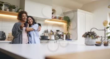 Loving Same Sex Mature Female Couple Wearing Pyjamas Hugging In Kitchen At Home Together