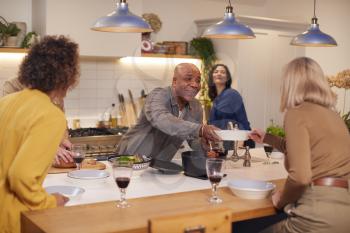 Group Of Mature Friends Meeting At Home Serving Food At Dinner Party And Drinking Wine Together