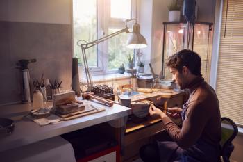 Male Jeweller Wearing Apron At Bench Working In Studio