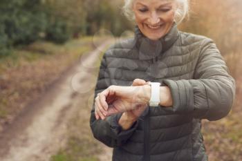 Senior Woman Running In Autumn Countryside Exercising Checking Smart Watch Fitness Activity App