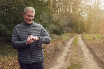 Senior Man Running In Countryside Exercising Checking Smart Watch Fitness Activity App