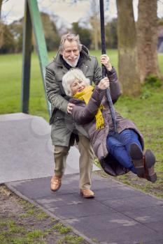 Senior Couple Having Fun Playing On Swing In Park Playground
