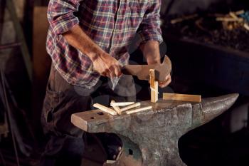 Close Up Of Male Blacksmith Chopping Wood For Kindling On Anvil To Light Forge