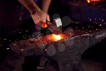 Close Up Of Male Blacksmith Hammering Metalwork On Anvil With Sparks