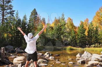 Gorgeous fall. Multi-colored autumn woods, mountains and river. The tourist in a white easy shirt admires beauty of a landscape
