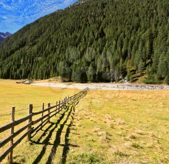 Scenic farm fields blocked bythe wooden fence. Shadow of the low fence beautifully lie on the grass. Alpine Valley in Austria. National Park Krimml waterfalls