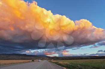 Summer rain. A huge rain cloud lit orange sunset. The cloud covers the sky over a gravel road. At the roadside parked jeep 