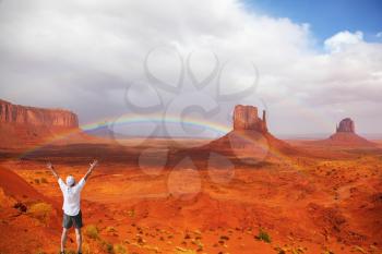 Enthusiastic tourist welcomes huge rainbow in Monument Valley. Navajo Indian Reservation, United States
