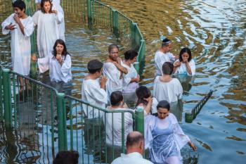 YARDENIT, ISRAEL - JANUARY 21, 2012: Christian pilgrims baptized in the Jordan River. They enter the water, dressed in special white robes