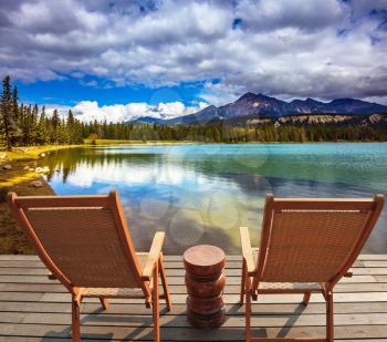 Two comfortable lounge chairs on wooden pedestal on the lake. Round lake in the coniferous forest. Canadian Rocky Mountains
