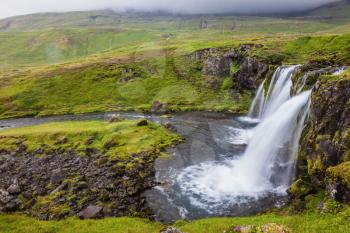 Foggy day in Iceland. Powerful cascading waterfall on the mossy cliff