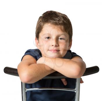 Picture taken on a white background. Very beautiful seven year old boy sits astride a chair