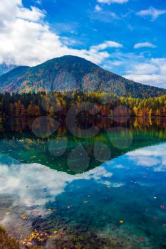 Scenic reflections of multicolored forests in water of the lake. Flood after rain. The quiet  Lago de Fusine, lake in Northern Italy. Concept of cultural and ecological tourism