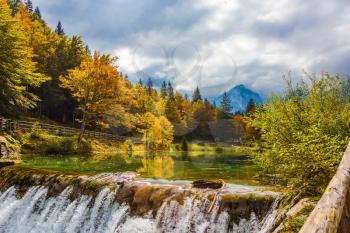  Concept of cultural, active and ecological tourism. Small waterfall on the picturesque quiet lake Lago de Fusine in the mountain valley. The beautiful forests. Flood after rain