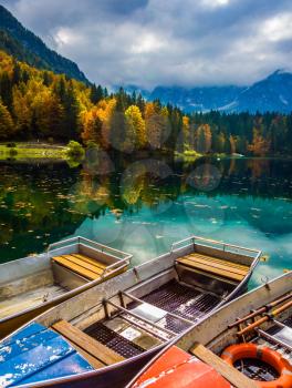  The picturesque multu-colored forests in the mountain Alpine valley. Boat station on the beautiful quiet lake of Lago de Fusine. Concept of cultural and ecological tourism