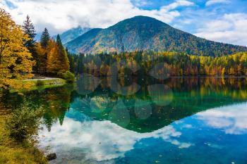 The quiet picturesque lake in Northern Italy, Lago de Fuzine. Picturesque reflections multi-colored the woods in smooth water of the lake. Concept of cultural and ecological tourism