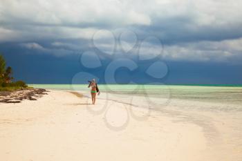 Young lady photographer in bikini walks on the caribbean tropical island sandy beach, Cuba vacation